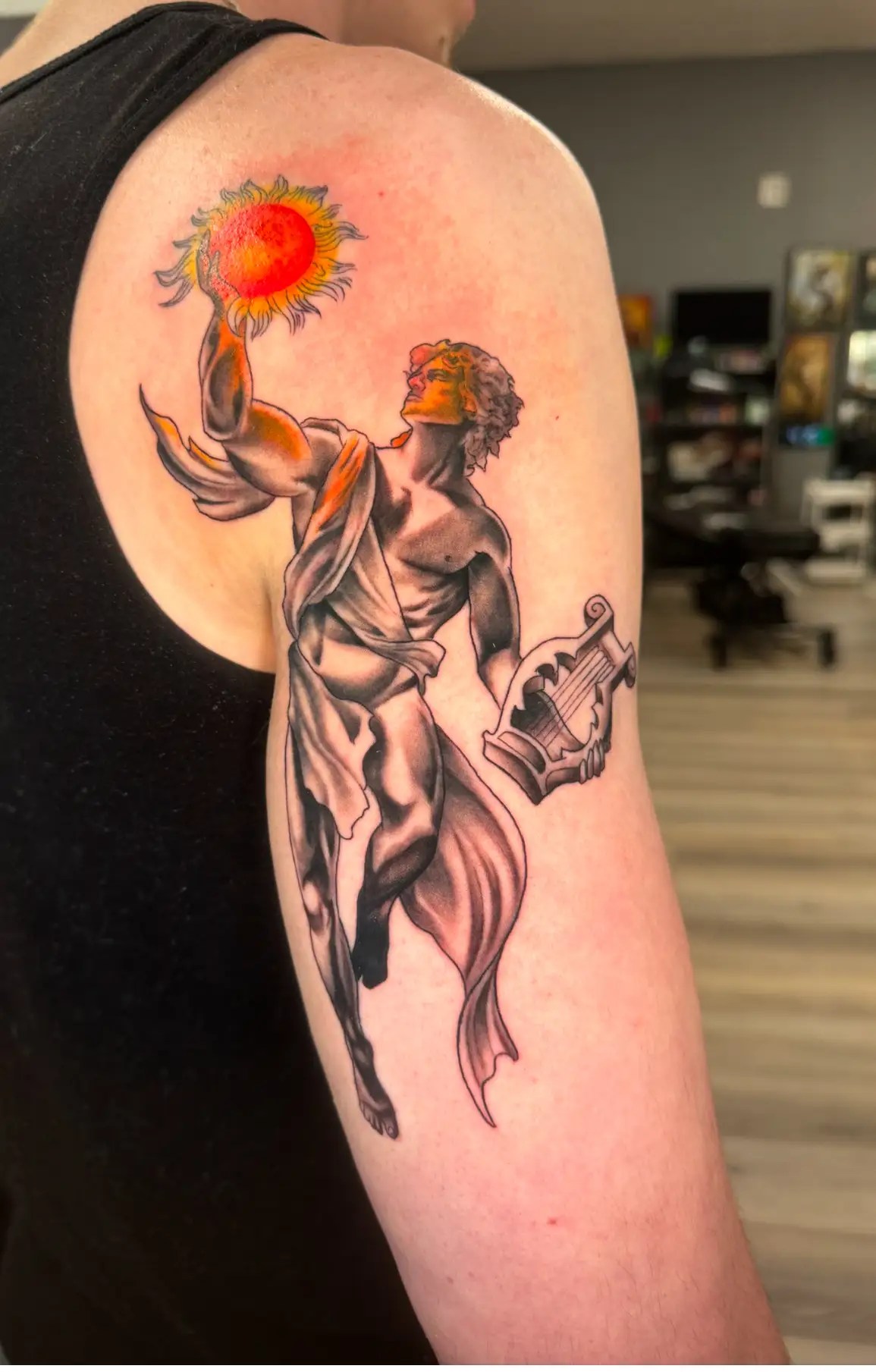 Black and grey tattoo of a man holding the sun and a harp
