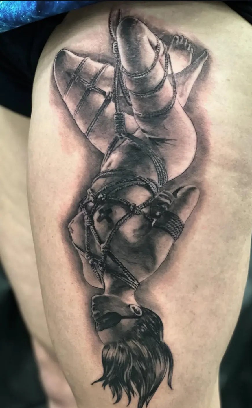 Black and grey tattoo of a woman tied up with ropes