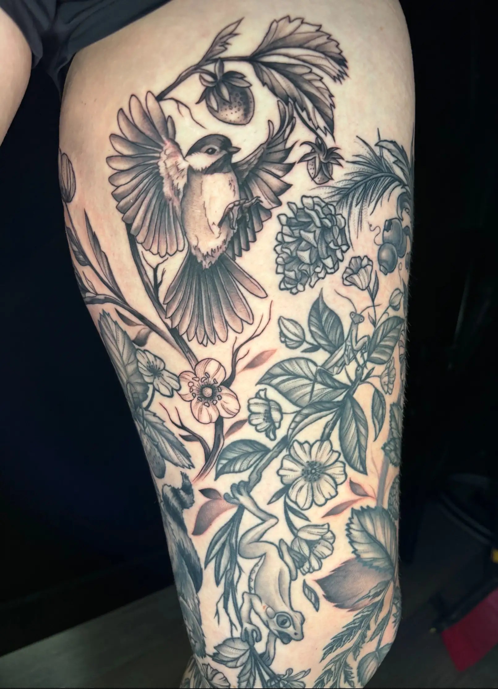 Black and grey realistic tattoo of flowers and small creatures