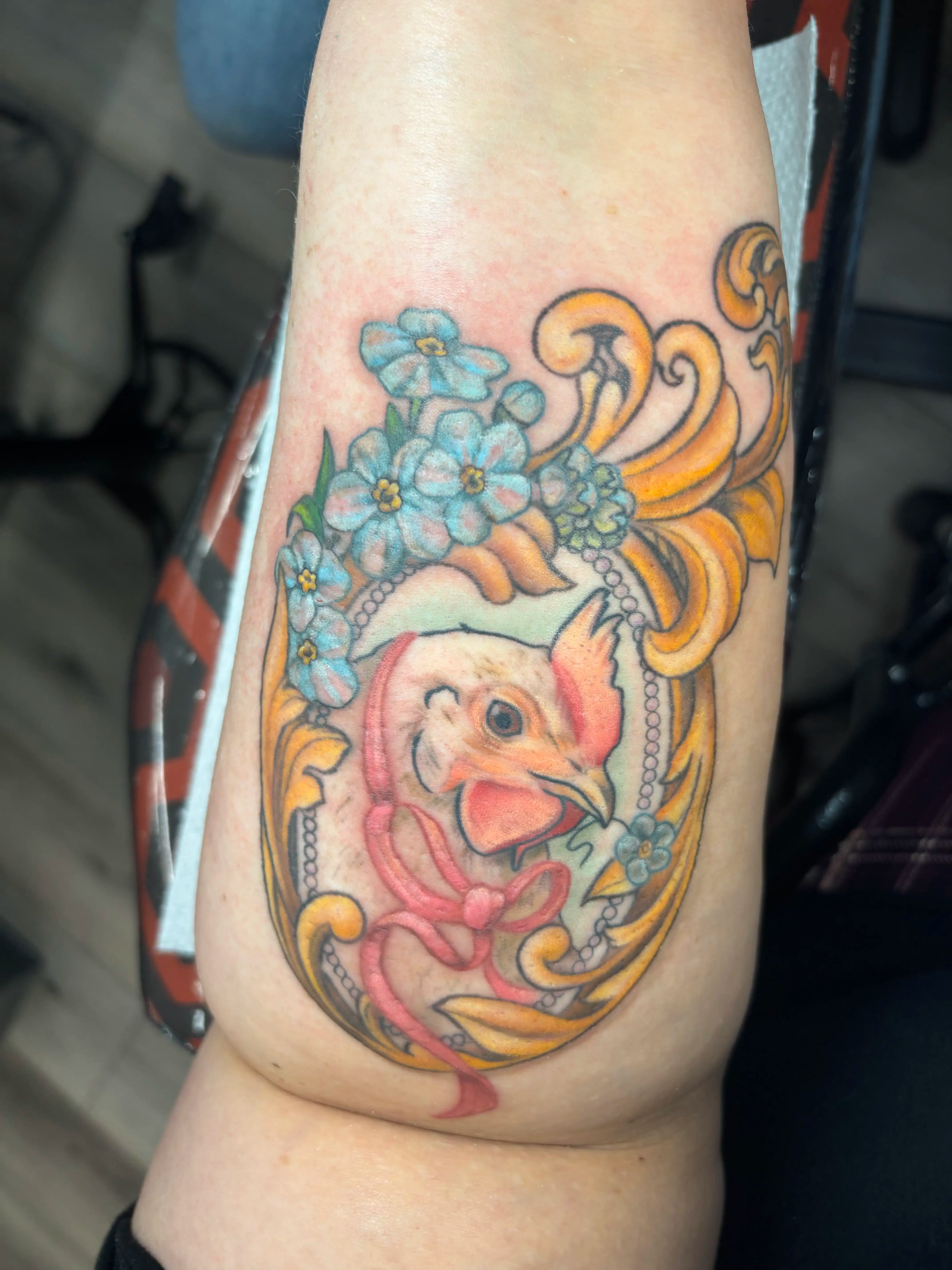 Realistic portrait tattoo of a chicken in a gold frame with flowers